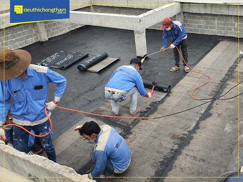 Kỹ thuật viên đang thực hiện khò nóng và trải màng chống thấm bitum khò nóng lên bề mặt công trình.